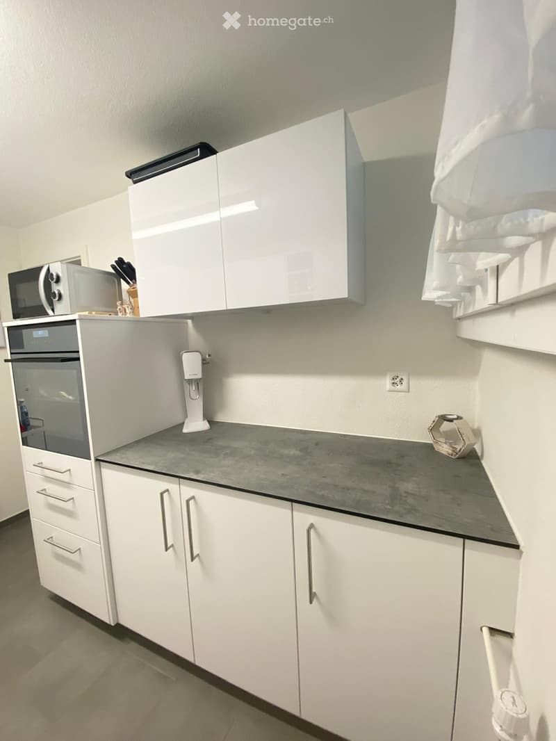 Modern kitchen with white cabinets, grey countertop, microwave, oven, and water dispenser.
