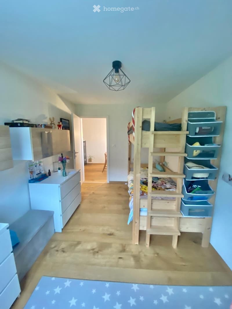 A cozy bedroom with a bunk bed, storage unit, and a small sitting area visible through an open doorway.