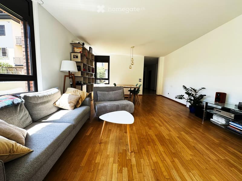 living room with wooden floor, gray sofa, white coffee table, white lamp, bookshelf, potted plant, dining table, chairs, large window