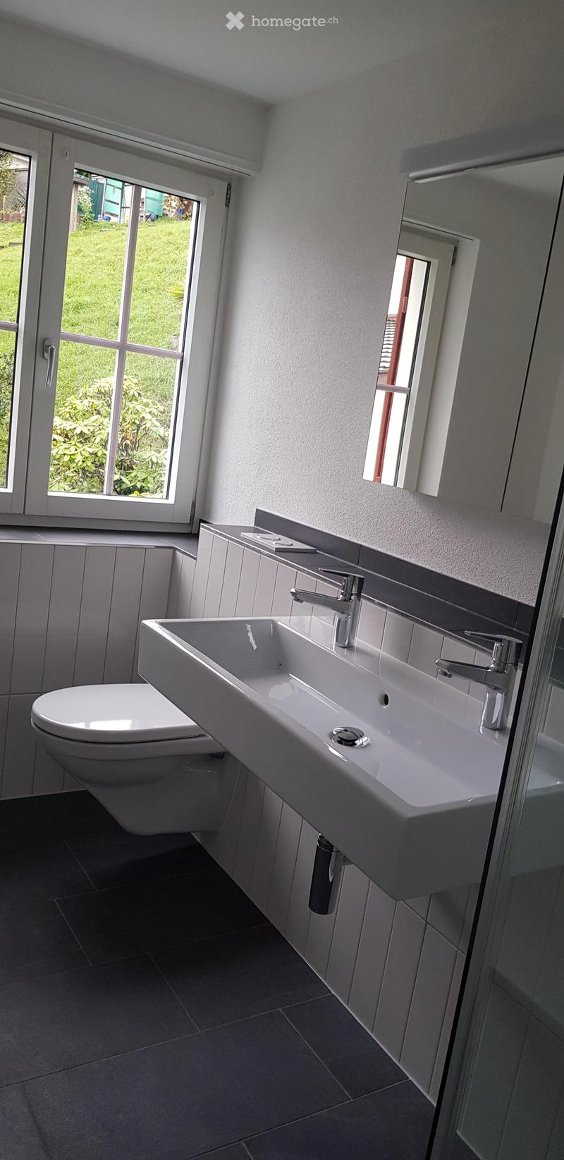 Modern bathroom with a white sink, chrome faucet, and large windows offering a view of the garden.