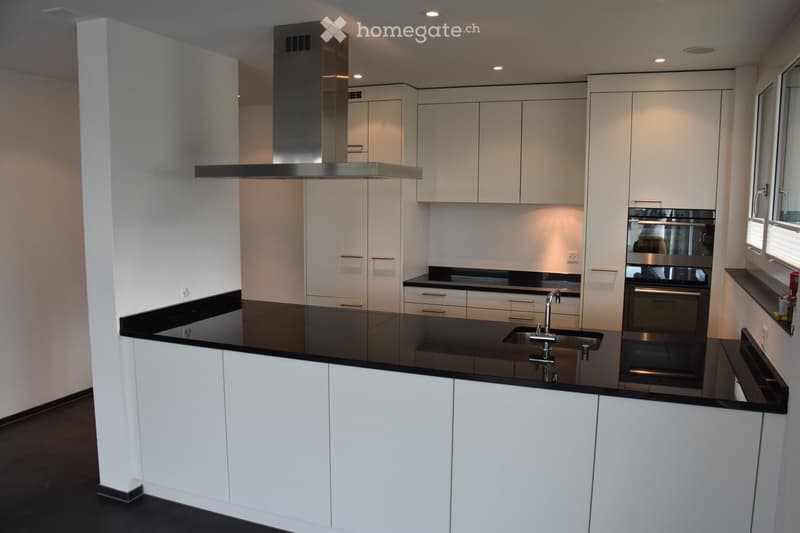 Modern kitchen with white cabinets, black countertops, stainless steel appliances, and a central island with a sink and faucet.