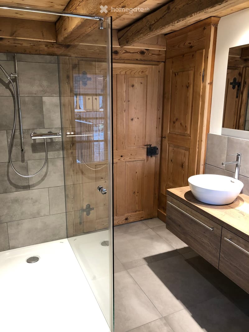 Modern bathroom with a large walk-in shower, glass enclosure, and a sleek sink with a modern faucet. Wooden cabinetry and exposed wooden beams on the ceiling.