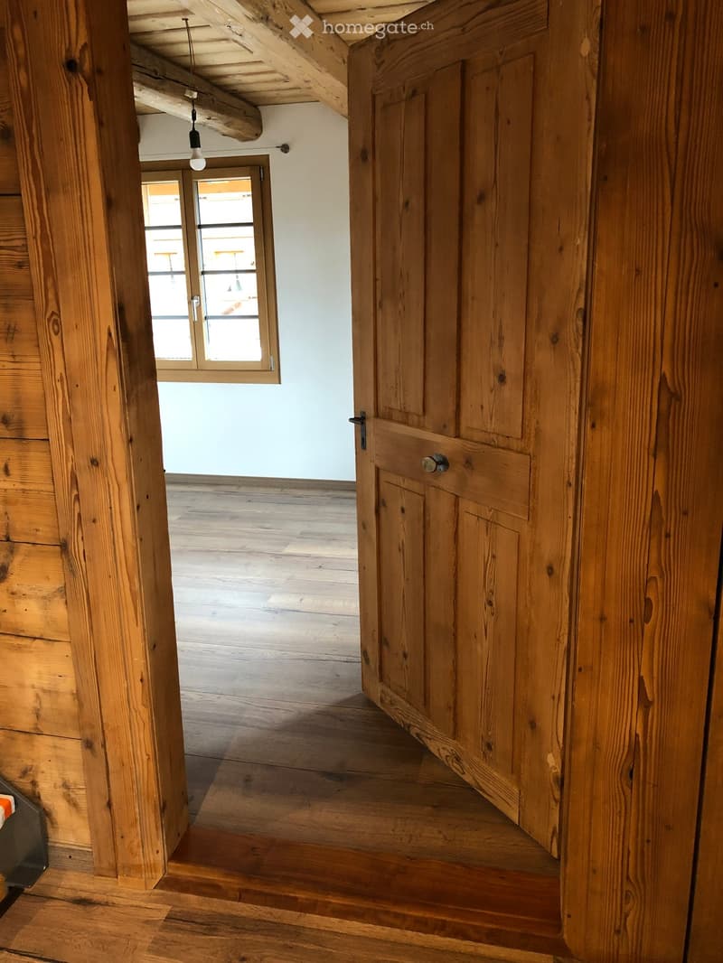 Wooden hallway with exposed beams, wooden floor, and a window leading to another room.