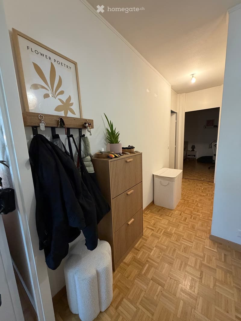Hallway with wooden flooring, coat rack with jackets, small storage cabinet, potted plant, and a trash bin. A sign reading "FLOWER POETRY" is mounted on the wall.