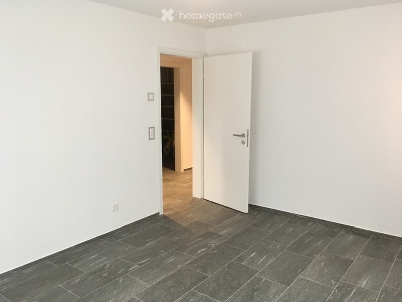 Empty room with dark grey tiled floor, white walls, and an open door leading to another room.