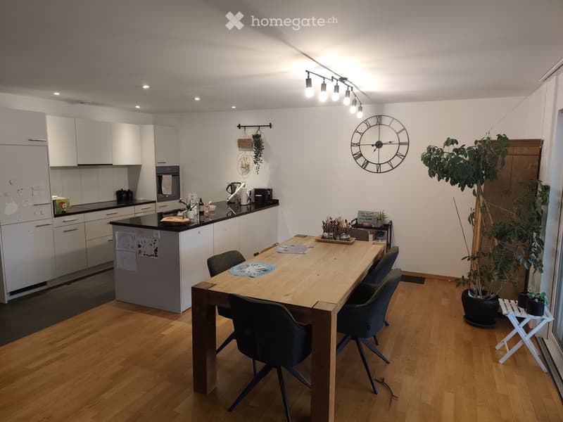Modern kitchen with white cabinets, a central island, a wooden dining table with chairs, and a large clock on the wall.