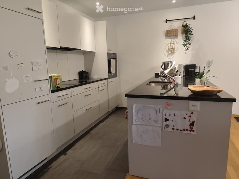 Modern kitchen with white cabinets, black countertops, stainless steel appliances, and a central island with drawings and magnets.