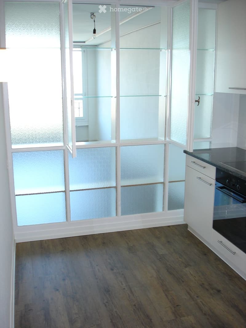 Empty room with wooden flooring, white walls, and large glass partitions. No furniture or appliances are present.