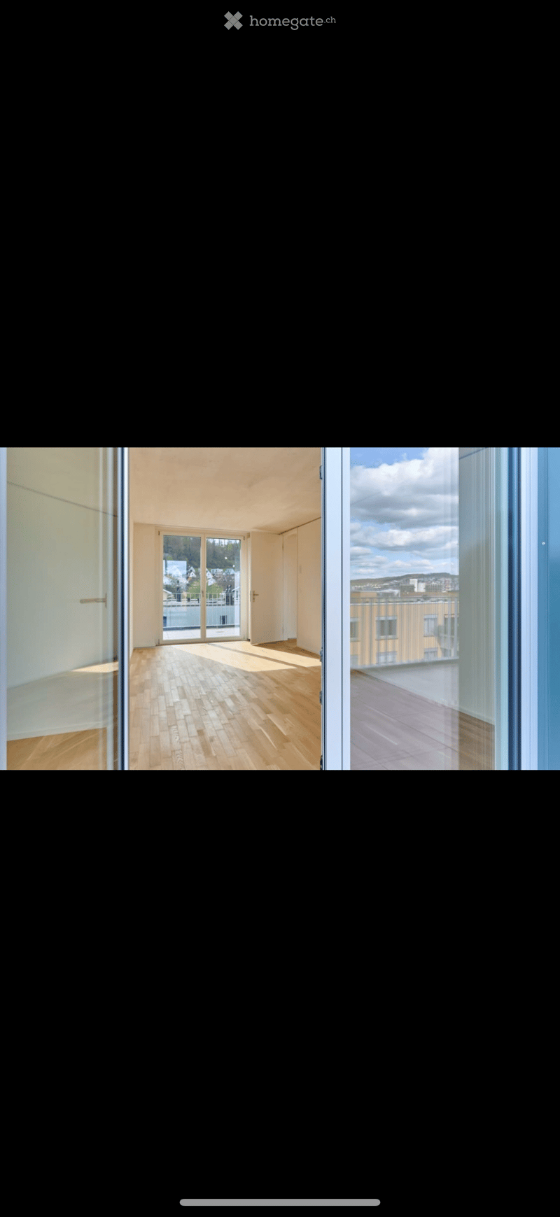 Empty room with wooden flooring, large windows, and sliding glass doors leading to a balcony or terrace.