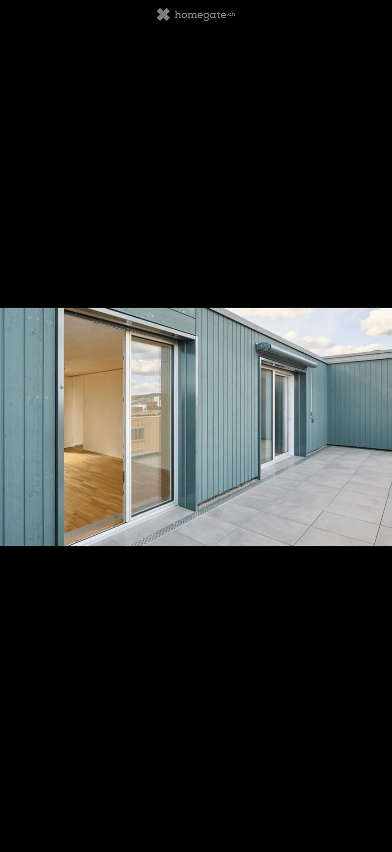 Modern rooftop terrace with light blue paneling, tiled floor, and large glass doors leading to an interior space with wooden flooring.