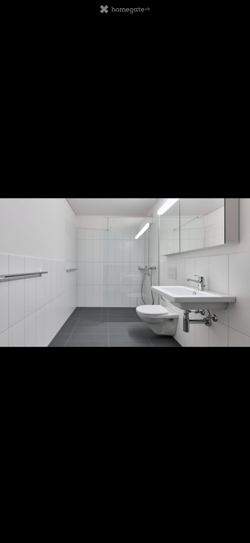 Modern bathroom with white tiles, dark grey floor, sink, toilet, mirror, and shower area.