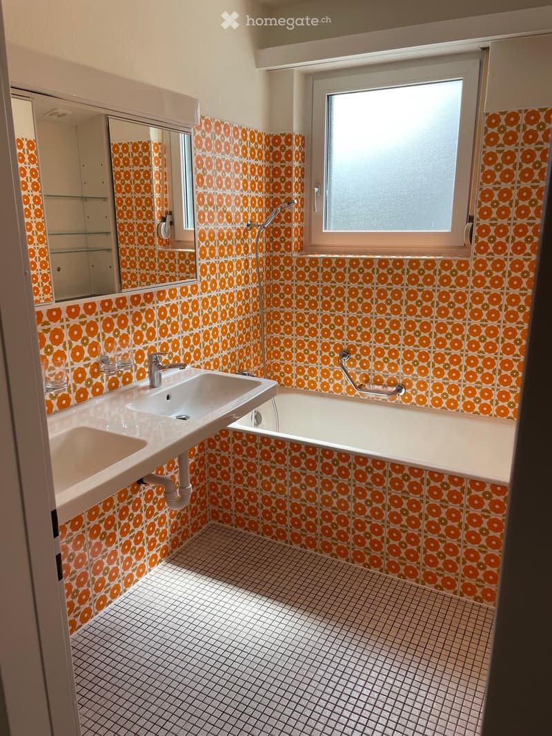 Bathroom with orange floral patterned tiles, white sink, bathtub, and mirror.