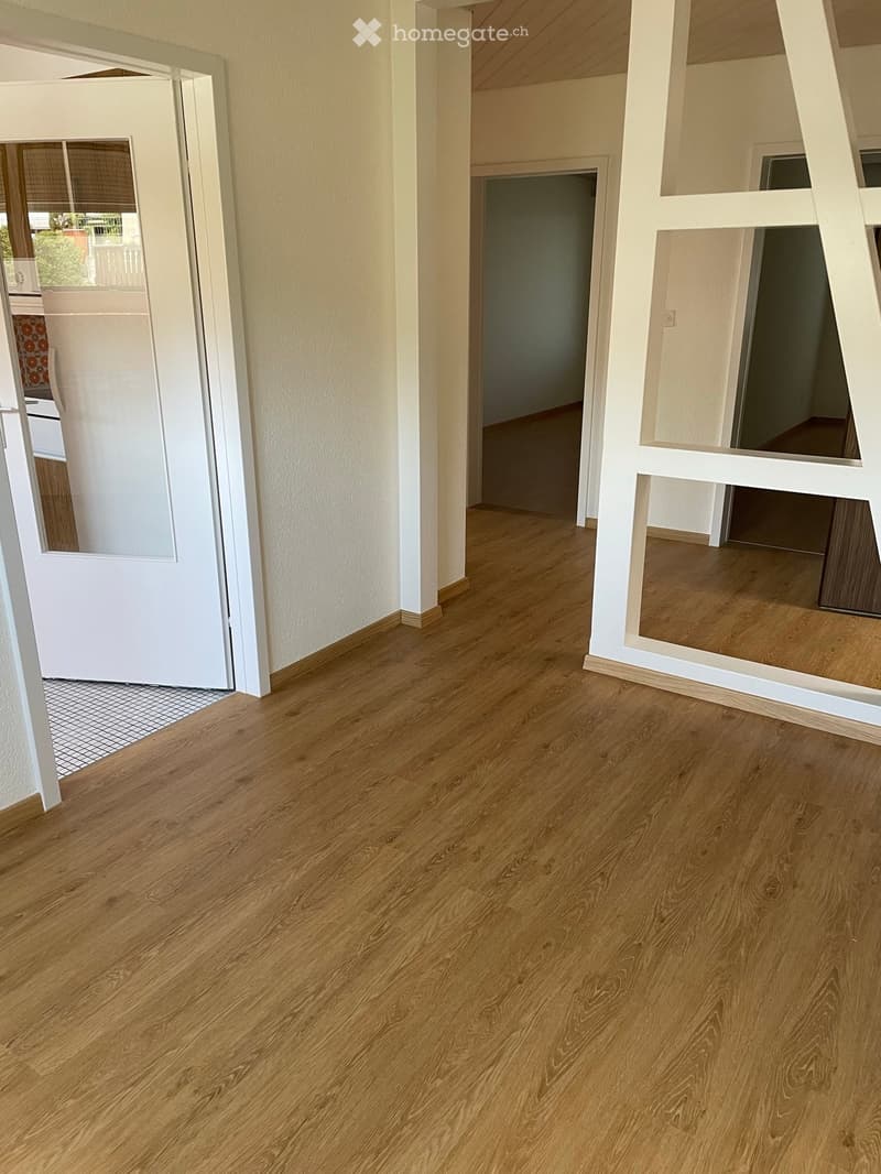 Empty hallway with wooden flooring, white walls, and a partially open door leading to another room.
