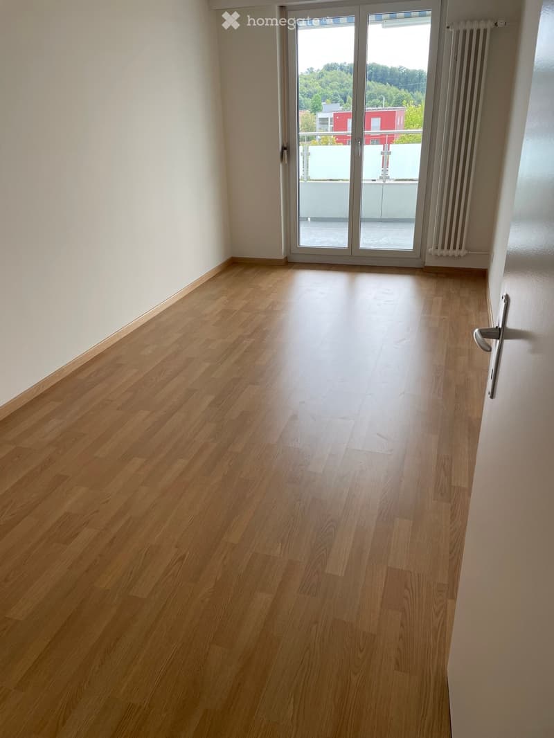 Empty room with light wooden flooring, white walls, and a large sliding glass door leading to a balcony.