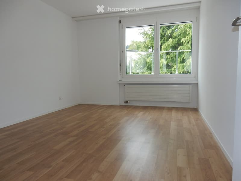 Empty room with wooden flooring, white walls, and a large window with a radiator below it.