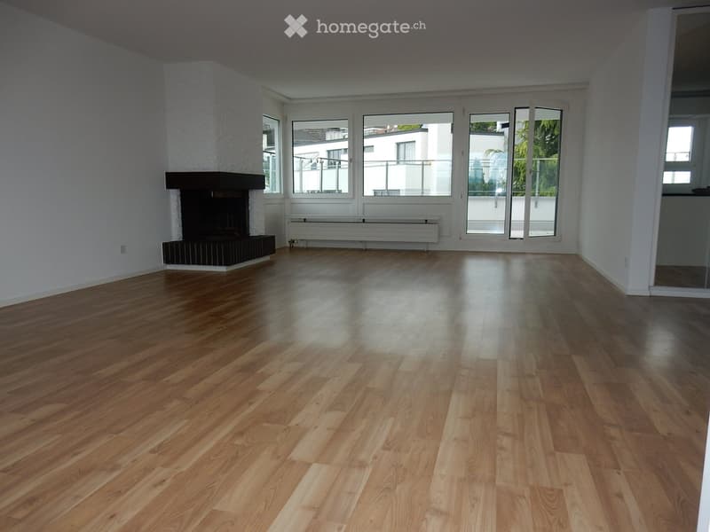 Empty room with wooden flooring, white walls, fireplace, large windows, and sliding glass doors leading to a balcony.