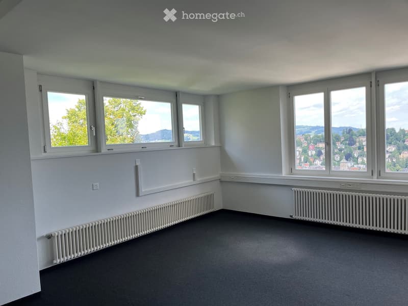 Empty room with white walls, large windows, radiators, and grey carpeted floor.