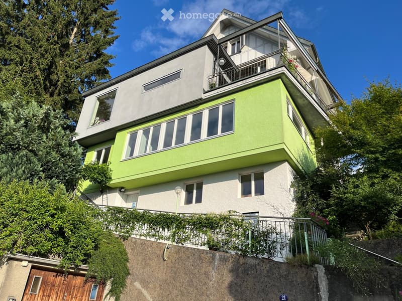 Two-story house with green and white exterior, large windows, and a balcony on the upper level.