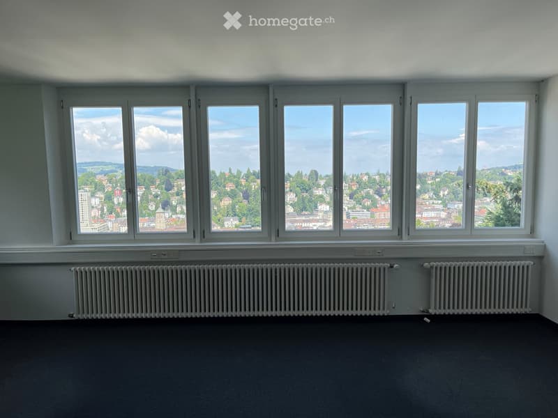 Empty room with large windows offering a scenic city view, radiators, and a dark carpeted floor.