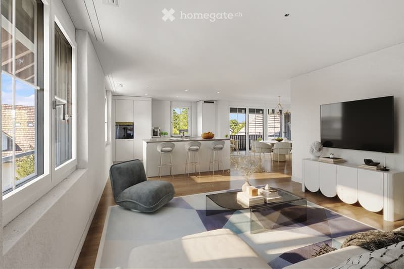 Modern living room with a grey sofa, coffee table, and a TV screen. The space includes a kitchen area with bar stools and a dining table, with large windows and a balcony view.