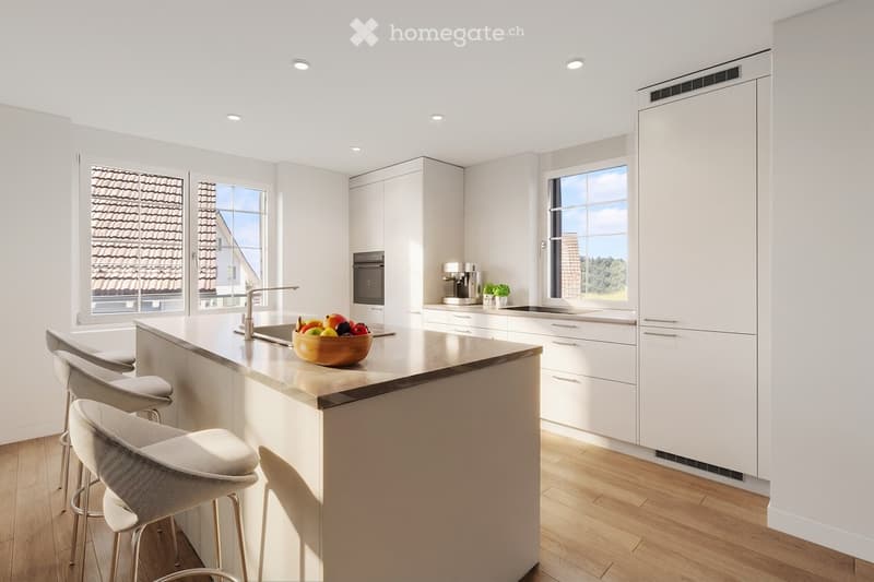 Modern kitchen with white cabinets, island, and wooden flooring. Features include a sink, oven, coffee maker, and a bowl of fruit on the island.