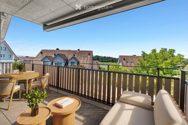 Balcony with a view of the surrounding houses and greenery, featuring a sofa, a dining table with chairs, and small wooden side tables with plants and a book.
