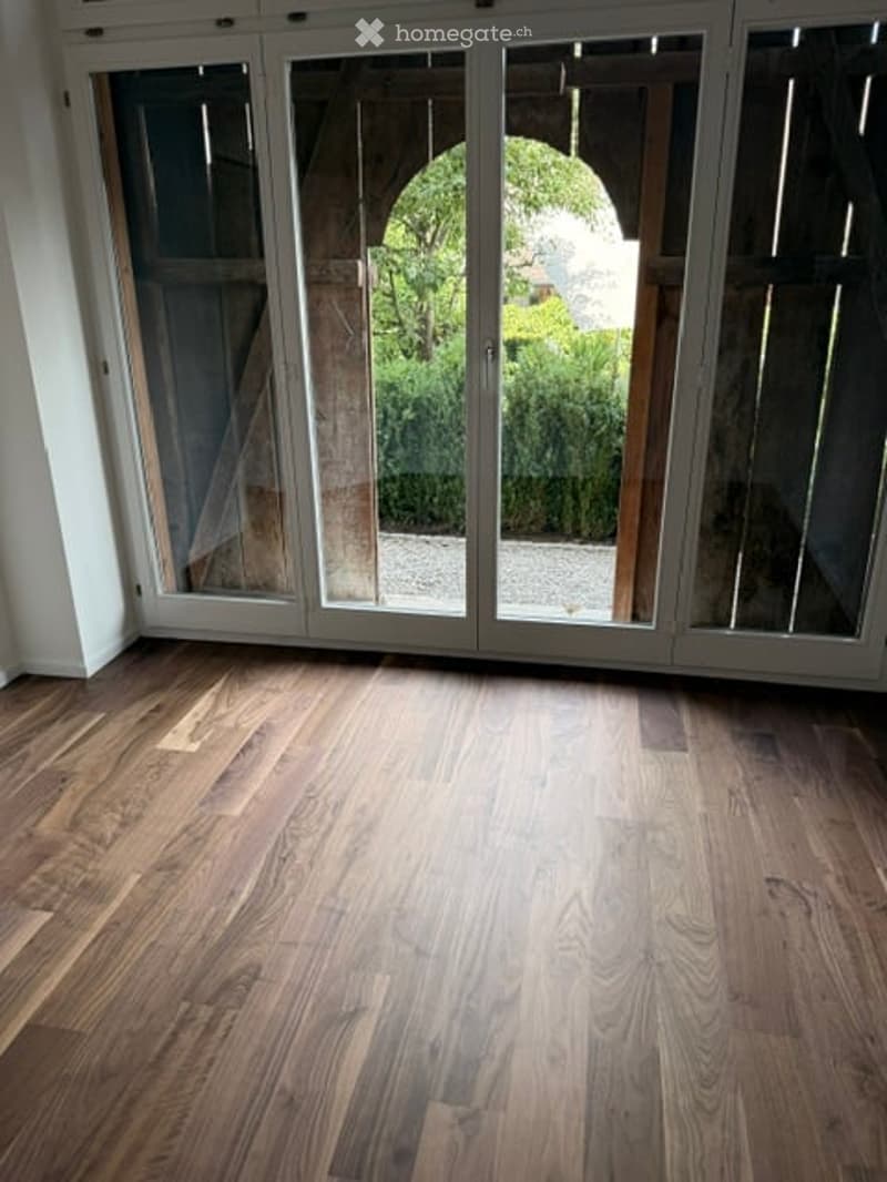 Empty room with polished wooden flooring and large glass sliding doors leading to an outdoor area.