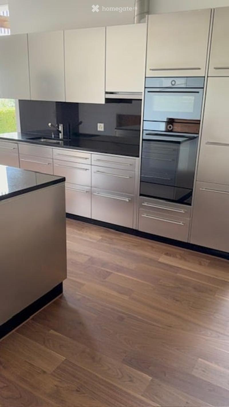 Modern kitchen with white cabinets, stainless steel appliances, black countertops, and wooden flooring.