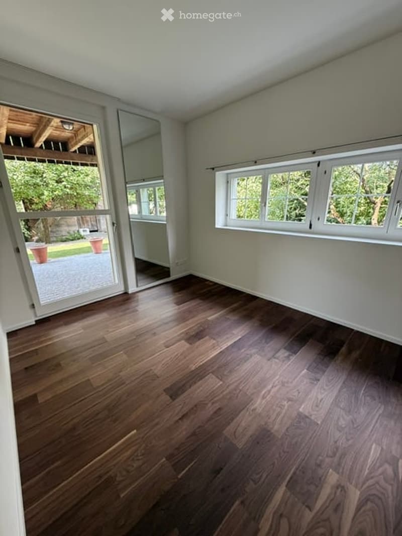 Empty room with wooden flooring, large windows, and sliding glass doors leading to an outdoor area.