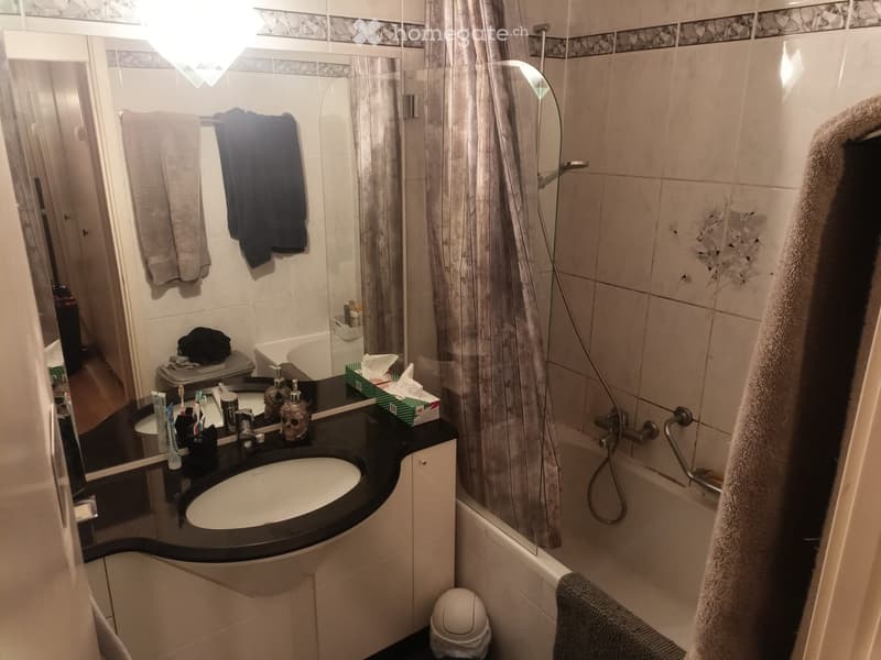 Modern bathroom with a black countertop sink, large mirror, bathtub with shower, and neatly arranged towels and toiletries.