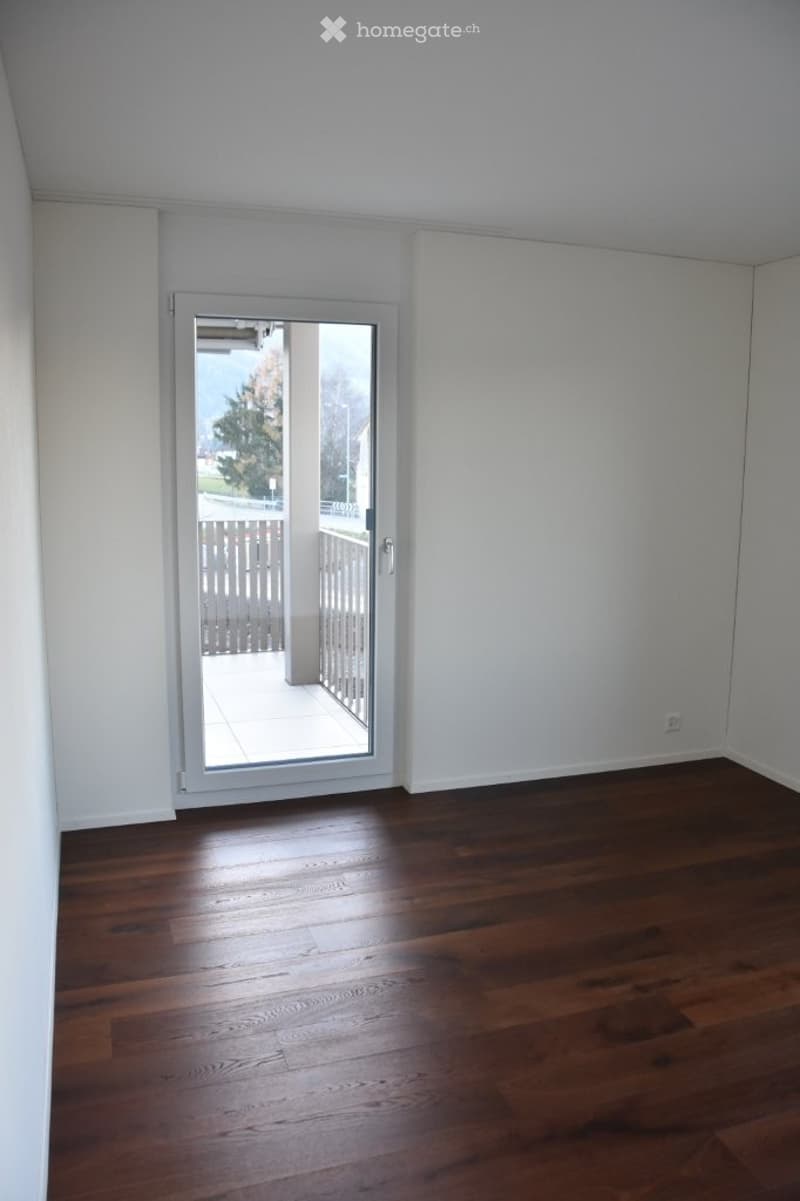 Empty room with wooden flooring and white walls, featuring a large glass door leading to a balcony.