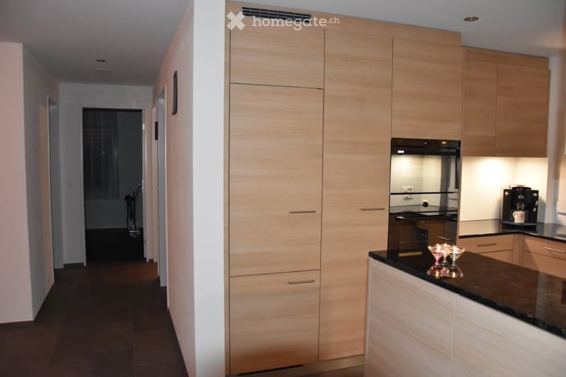 Modern kitchen with light wood cabinets, black countertop, built-in oven, coffee maker, and decorative bowl on the counter.