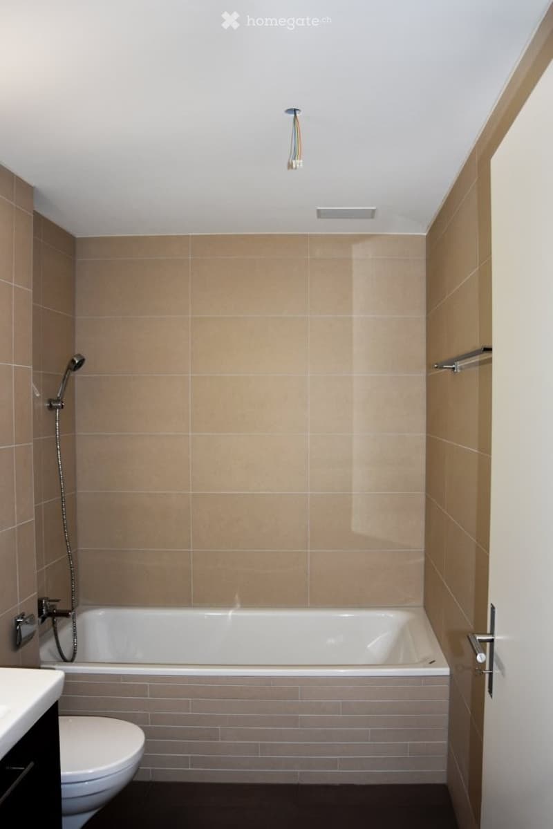 Modern bathroom with beige tiled walls, a white bathtub, a toilet, a showerhead, and a towel rack.