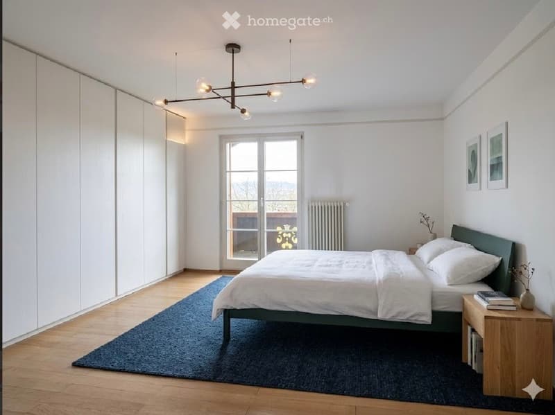 Modern bedroom with a large bed, nightstand, books, vase, picture frames, radiator, and a wardrobe. The room features wooden flooring, white walls, and a large window with a view of the outdoors.