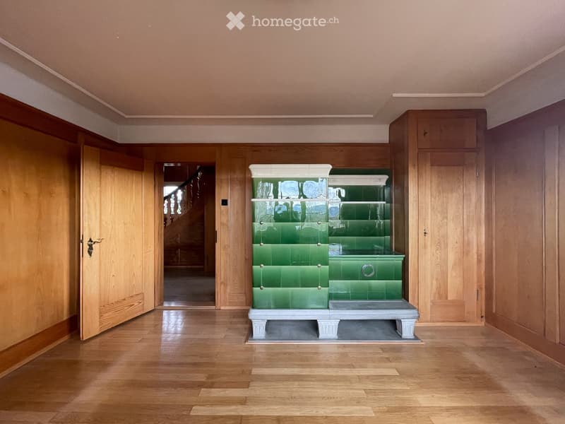open room with wooden floor, wooden walls, open door to another room, green tiled fireplace