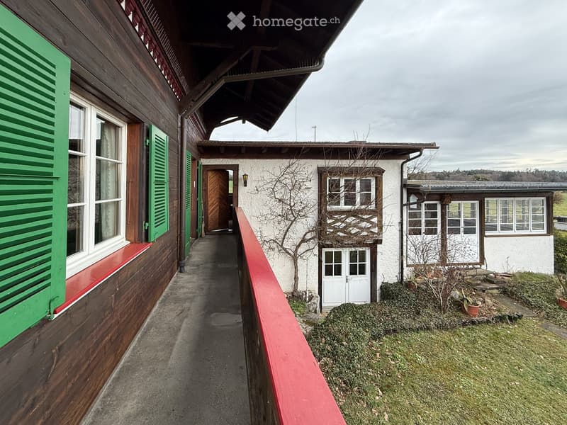 A wooden house with a balcony, green shutters, and a red railing.
