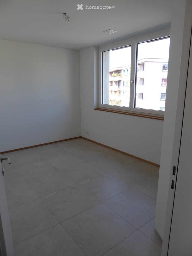 Empty room with tiled floor, white walls, large window with wooden sill, and visible electrical outlet.