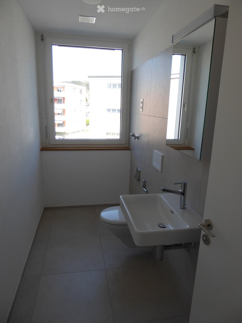 Modern bathroom with a white sink, chrome faucet, toilet, and large windows offering a view of the building exterior.