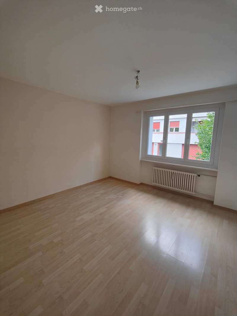 Empty room with wooden flooring, white walls, and a large window with a radiator below it.