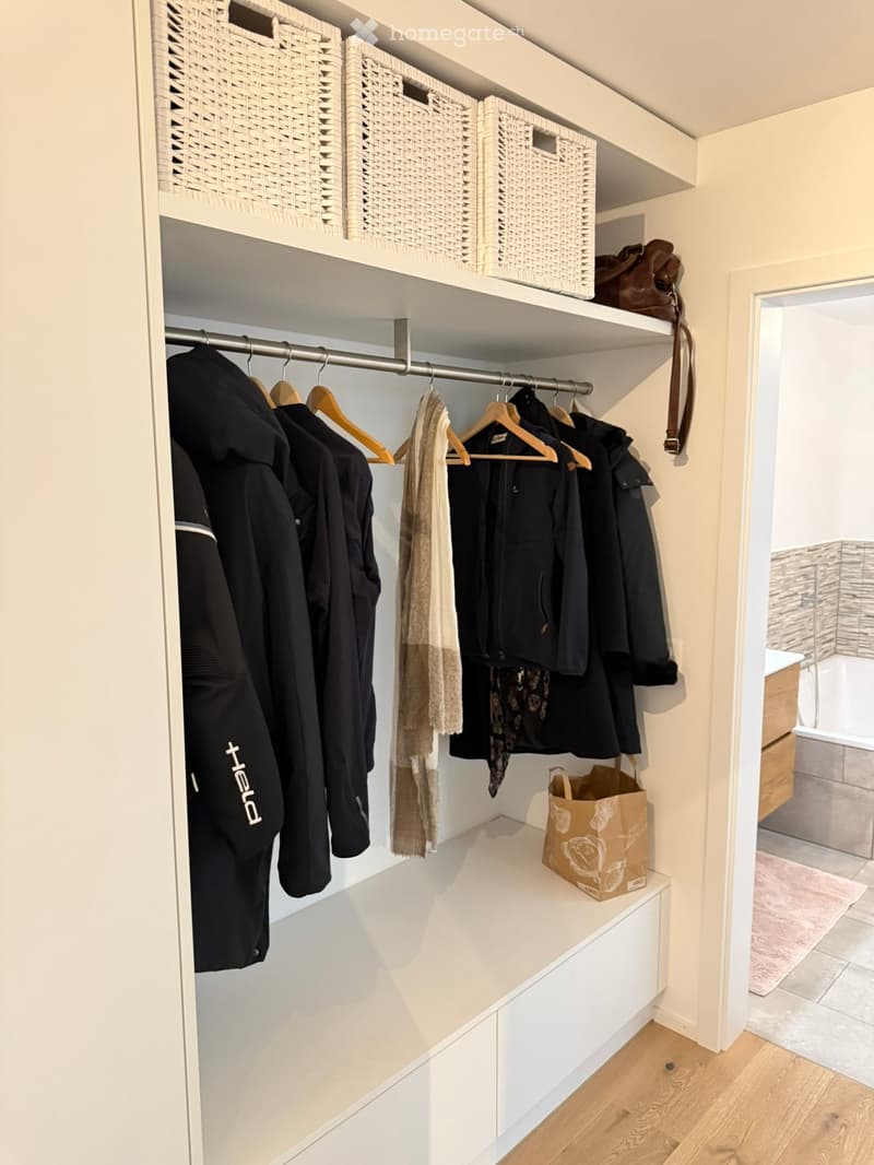 Well-organized walk-in closet with built-in shelving, hanging rods, and storage baskets. Contains clothing, scarves, and a handbag.
