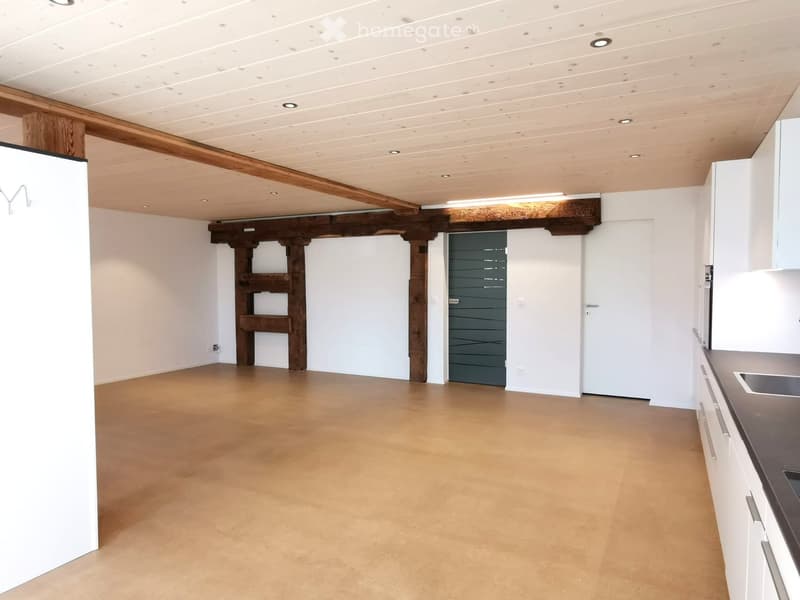 Empty room with exposed wooden beams, white walls, and a concrete floor. Features a white cabinet and a sink in the corner.