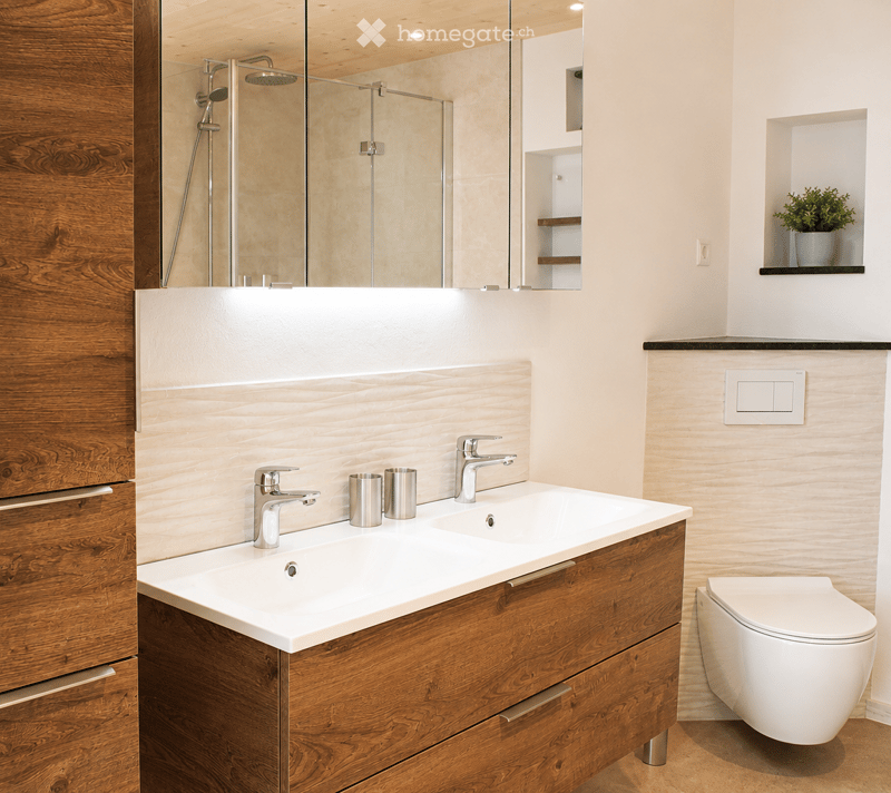 Modern bathroom with a double sink, wooden vanity, sleek chrome faucets, a large mirror, a glass-enclosed shower, and a toilet.