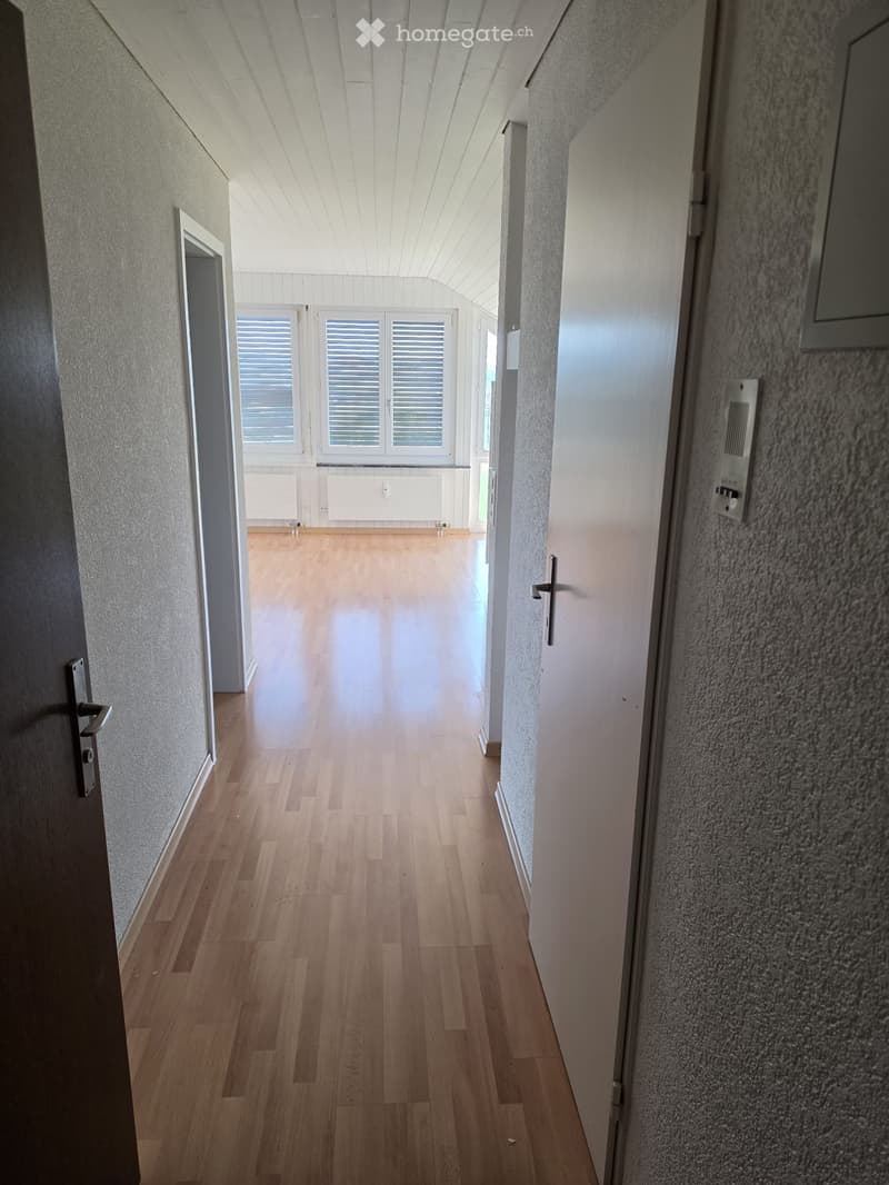 Empty hallway with wooden flooring, white walls, and a window at the end.