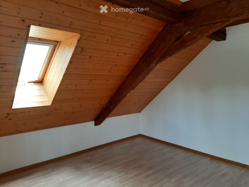 Empty attic room with wooden walls, exposed wooden beams, and a skylight window allowing natural light to enter.