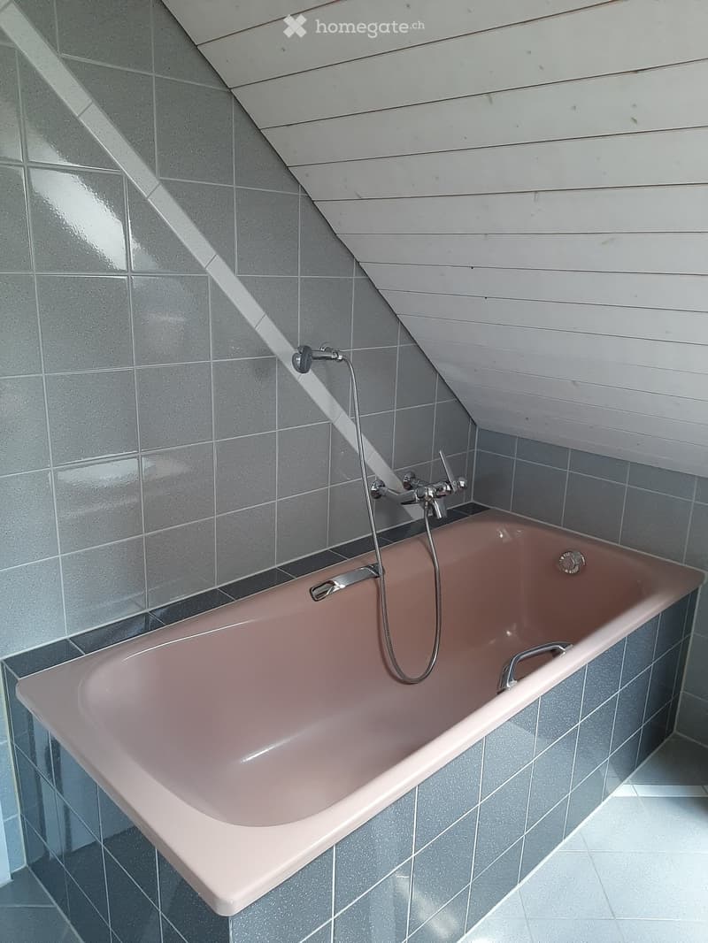 Modern bathroom with a pink bathtub, grey tiled walls, and a sleek chrome faucet.