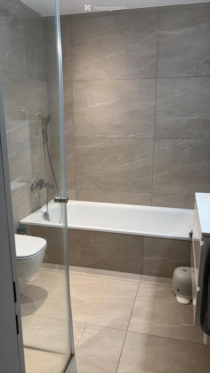 Modern bathroom with marble tiles, a bathtub, toilet, and a glass-enclosed shower area.
