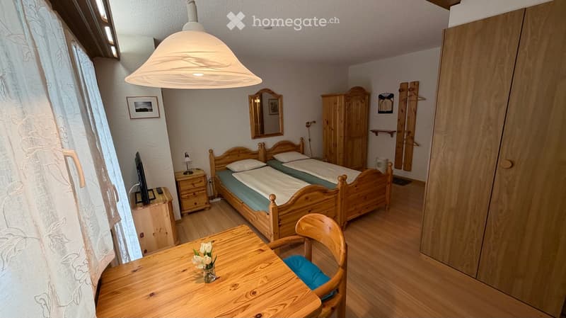 Cozy bedroom with wooden bed, nightstand, table, chair, wardrobe, and mirror.