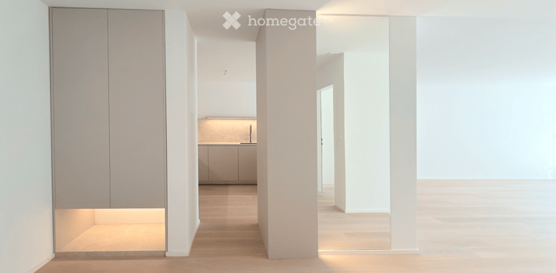 Open, minimalist corridor with white walls, wooden flooring, and recessed lighting. No furniture or equipment visible.