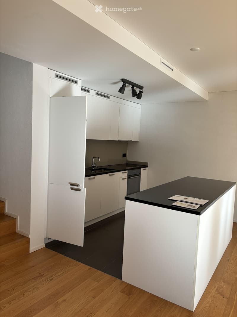 Modern kitchen with white cabinets, black countertops, and a central island. Features include a sink, faucet, and built-in lighting.