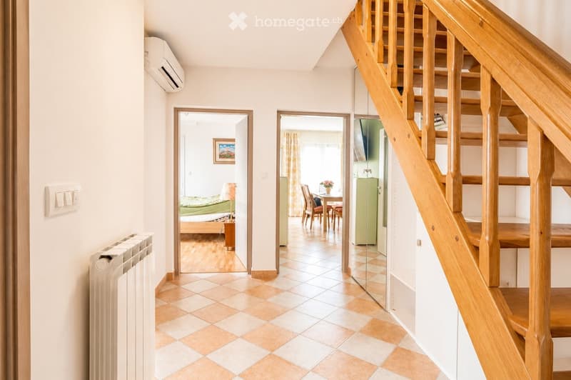 Bright hallway with tiled floor, wooden staircase, and open doors leading to a bedroom and dining area.